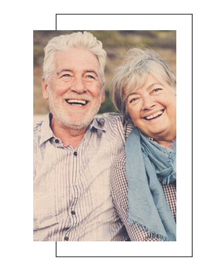The image shows an elderly couple smiling at each other with the man on the left and the woman on the right. They are standing close together, and both appear happy.