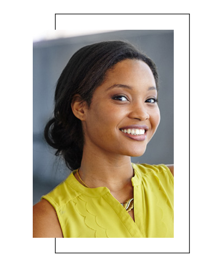 The image shows a woman with a radiant smile, wearing a yellow top and a light-colored blouse, against a blurred background.