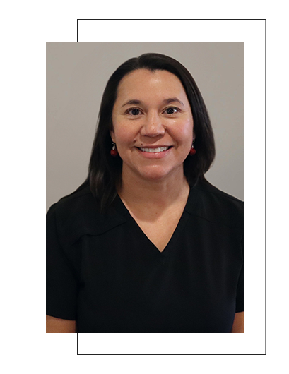 The image shows a person smiling at the camera, wearing a dark top with a name tag, set against a plain background.