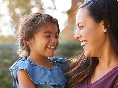 A woman is smiling at a child while standing outdoors during daylight.