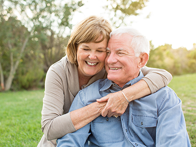 An elderly couple embracing each other outdoors during sunset.
