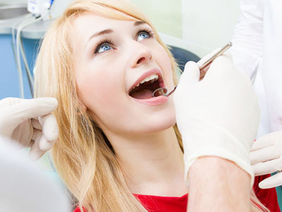 A woman receiving dental treatment with an open mouth, wearing red shirt, while a dentist works on her teeth.