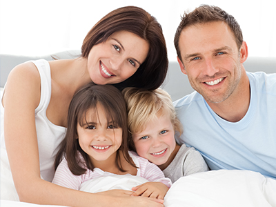 A family of four posing together on a bed with a smile.