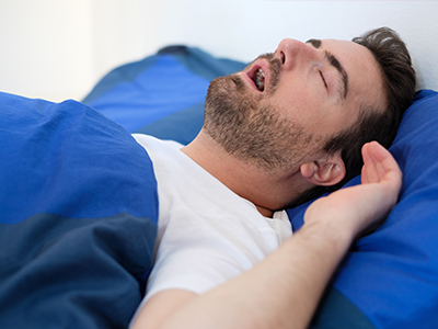 The image shows a man lying down with his eyes closed on a bed with blue bedding.