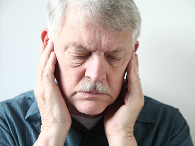 The image shows a man with his hand on his face, appearing to be in pain or discomfort, with a serious expression.